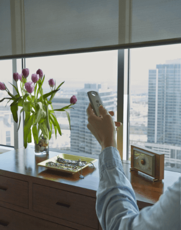 Modern living room with a large window showcasing sleek, motorized shades. The shades are open, revealing a view of the city