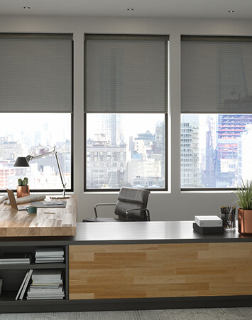 Office with sleek black roll-up shades on large windows.