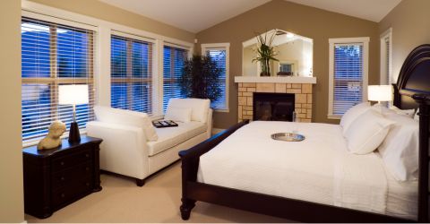 Nighttime ambiance in a luxurious bedroom with fireplace and king-sized bed, accented by sleek white vinyl blinds