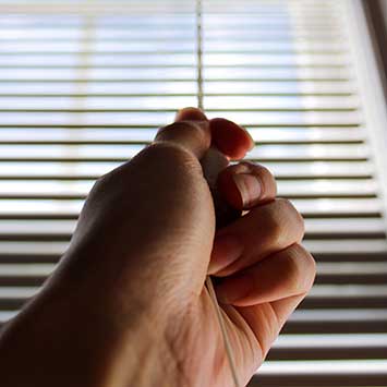A hand using a cord to open aluminum blinds