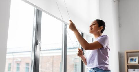 A woman is opening window roller shades